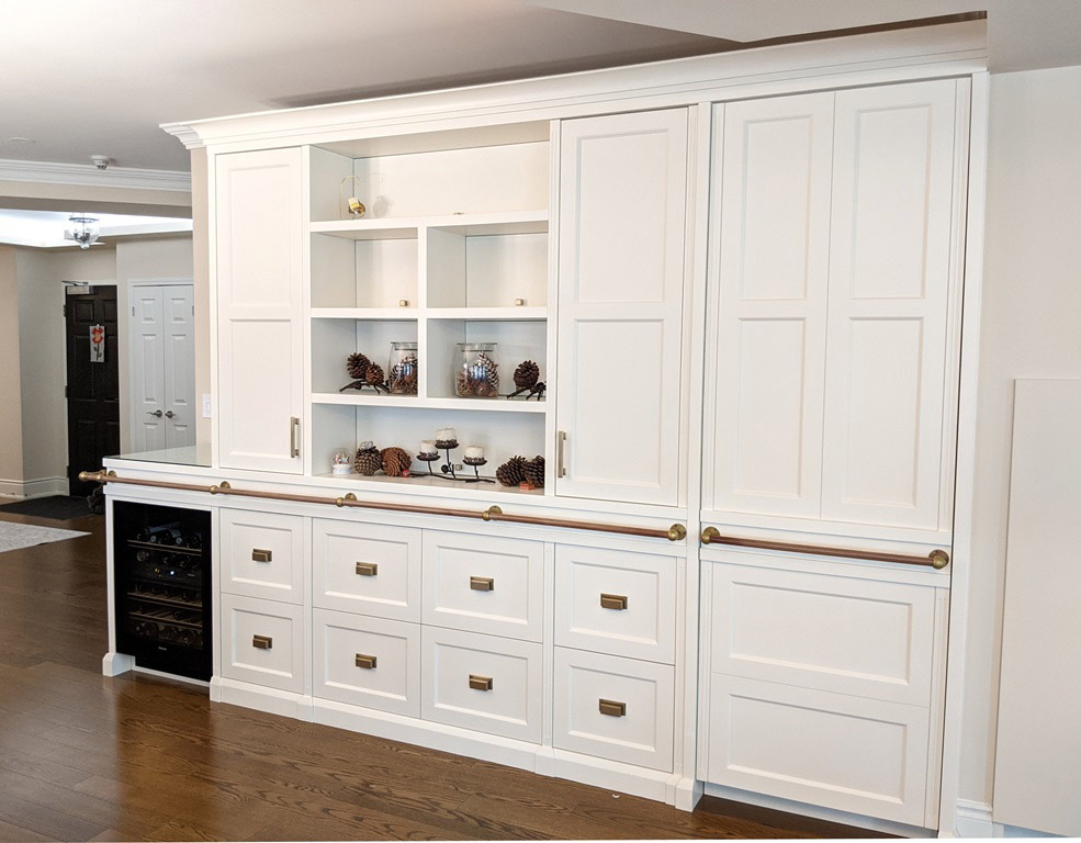 Transitional style white custom-built cabinetry with bar fridge, built in freezer, open bookshelf, closed storage and decorative railing.