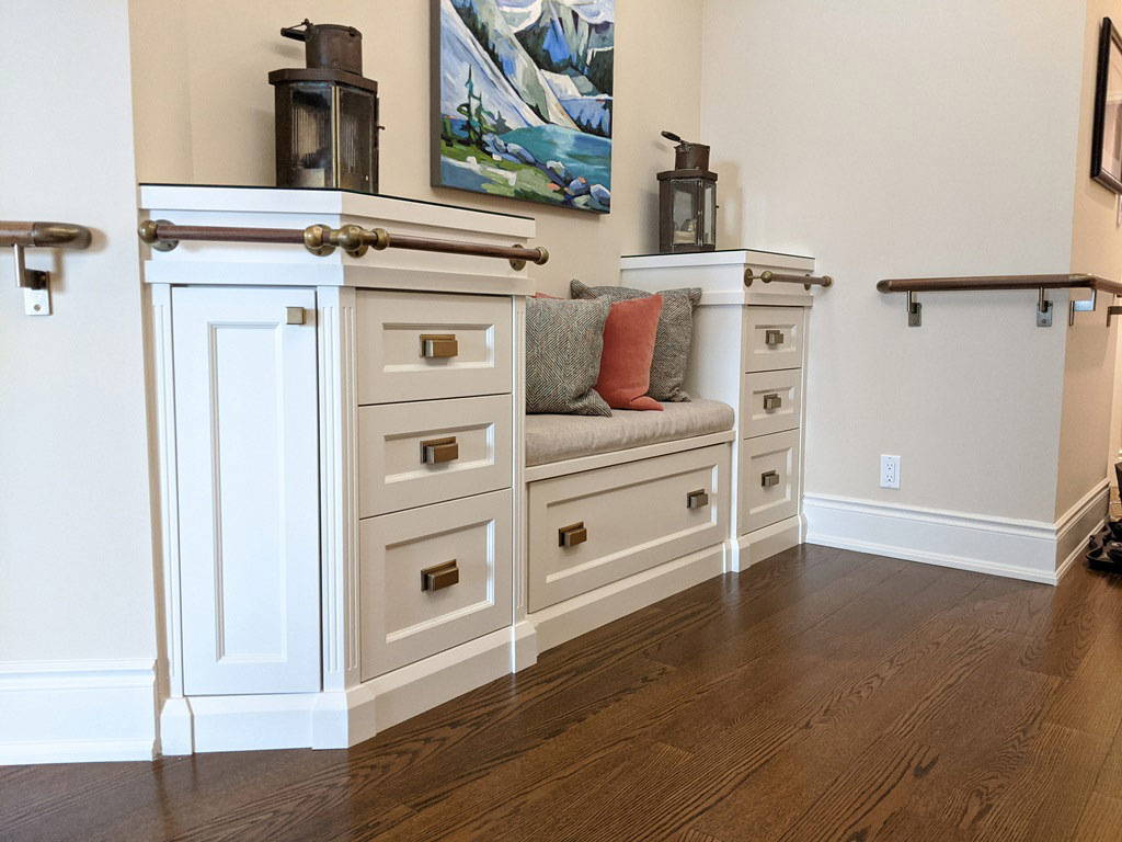 Transitional style white custom front entry cabinet with built in bench seating, decorative railing, and drawer storage.