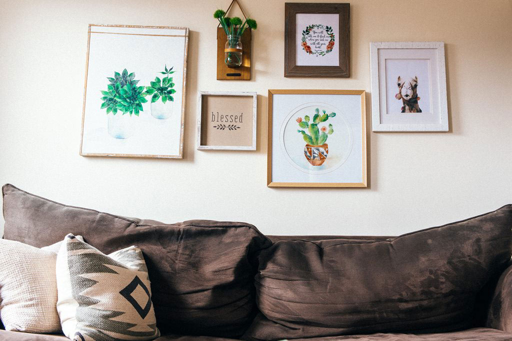 The back pillows of a brown sofa with framed art and quotations.