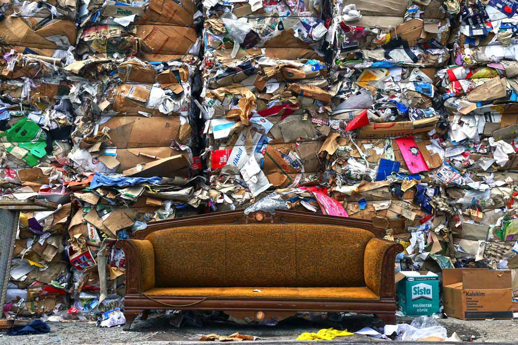 A traditional sofa sitting outside with piles of garbage stacked behind it.