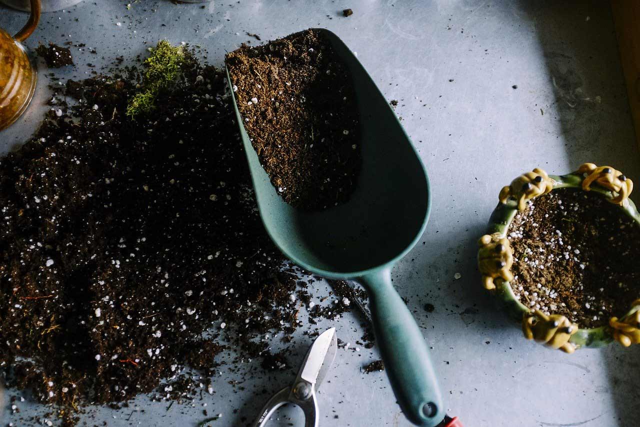 A large scoop partially filled with soil sits on top of a table with more soil.