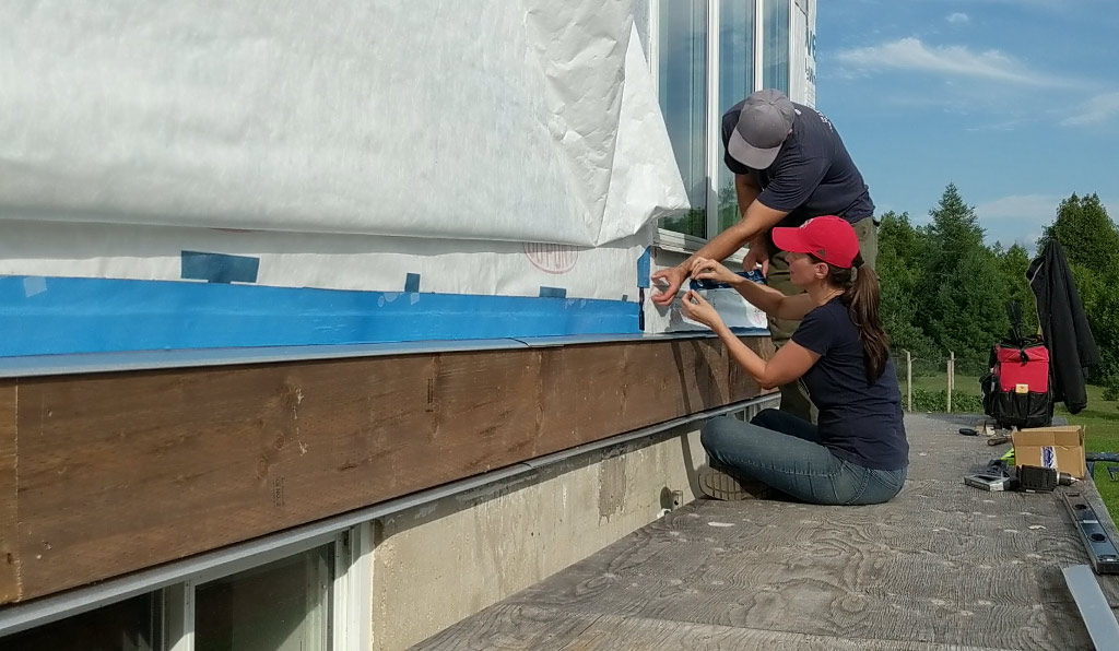 A photo of Justin and Celia working together on waterproofing under a large window.