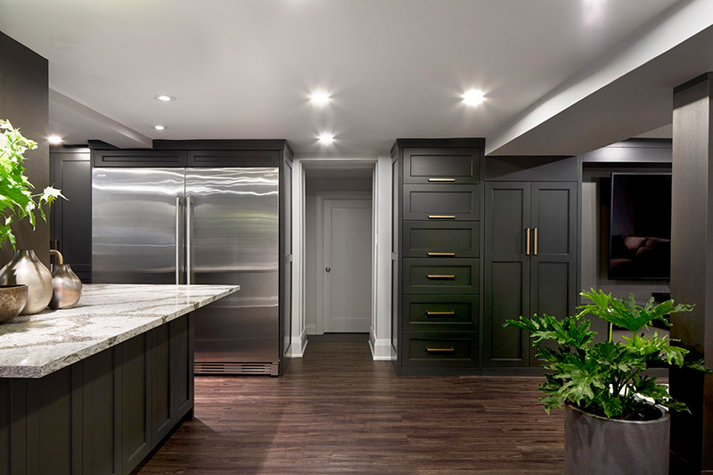 Dark grey custom cabinetry with brass handles, a dark walnut flooring, a large double sided fridge freezer, and a green plant in a grey pot