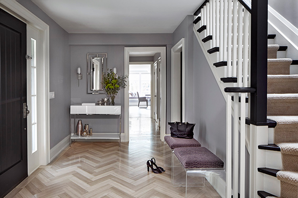 A front entry designed in purple and purple grey with a white front entry table, a black front door and a herringbone tile pattern on the floor.