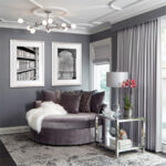 A reading nook designed in shades of purple grey with artwork on the walls, a large round reading chair, a side table, floor to ceiling drapery and an area rug.